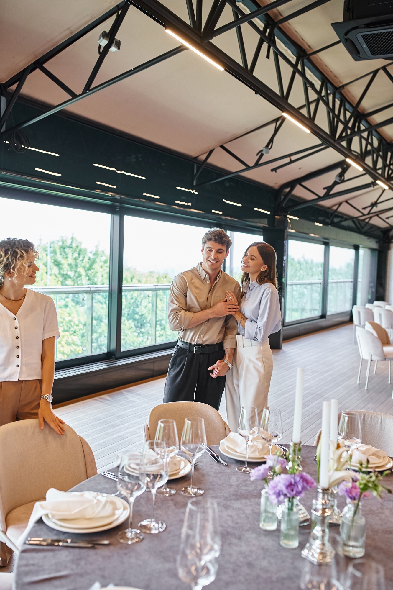 smiling couple in love looking at decorated festive table near wedding coordinator in event hall