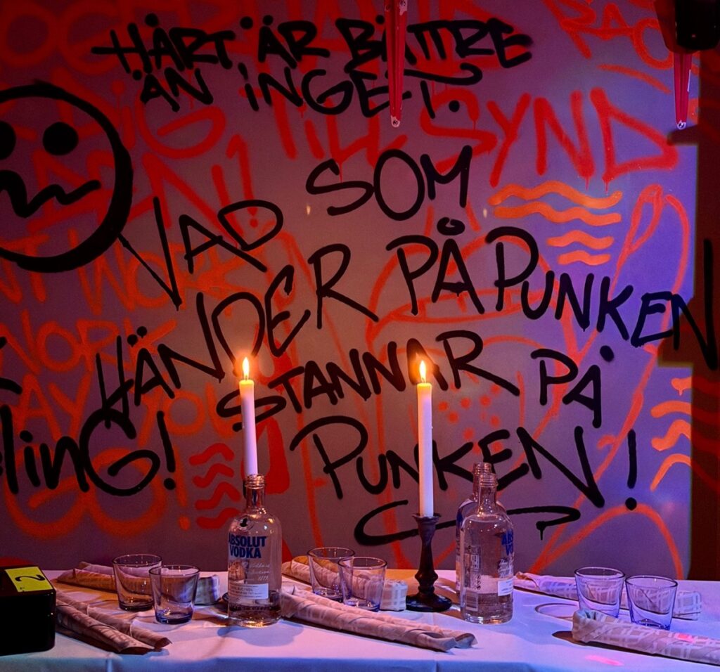 Röd graffitivägg med texten Vad som händer på Punken stannar på Punken, framför ett dukat bord med tända ljus